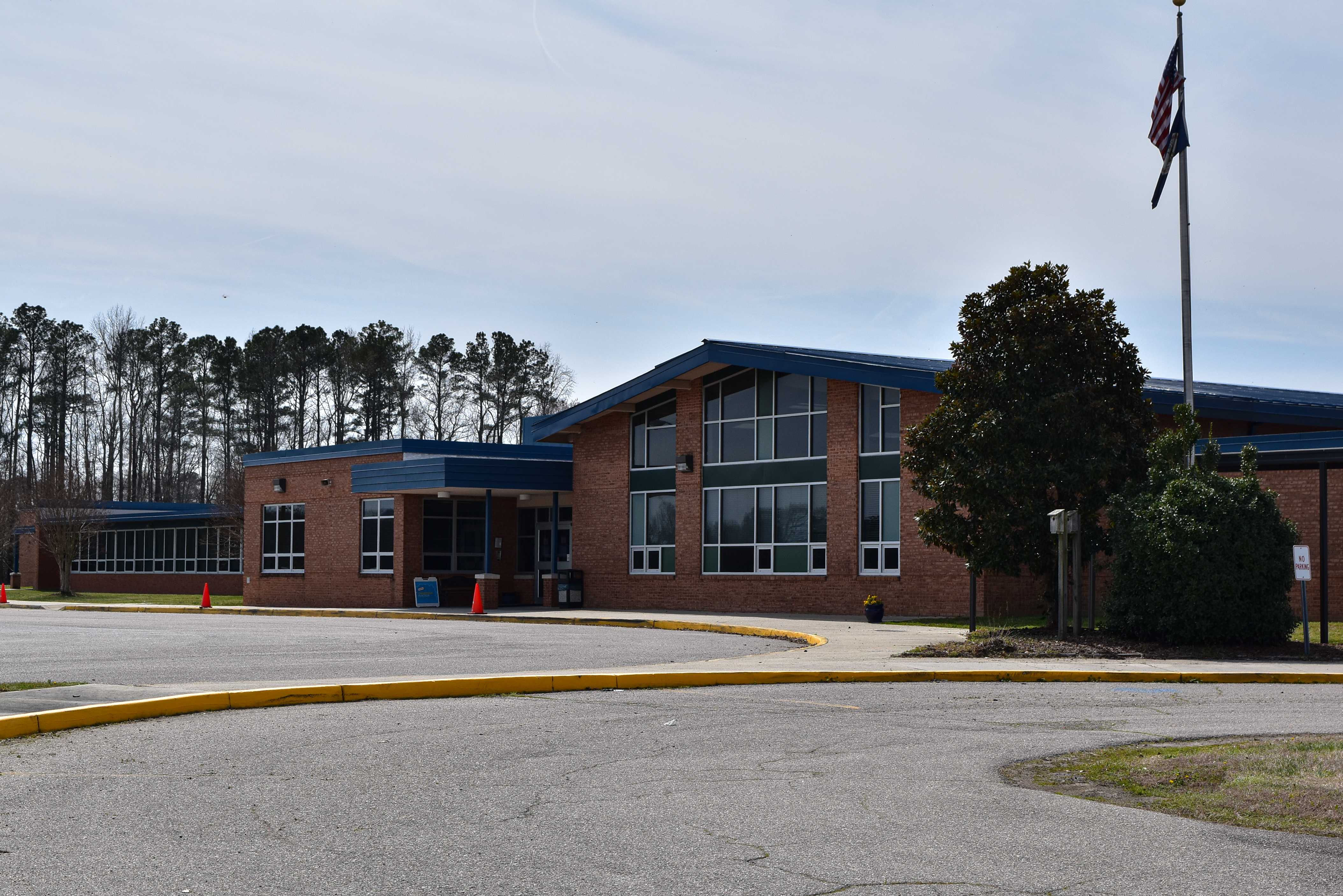 The campus of the school, featuring a brick school building, a blue trimmed roof, and accent trees.